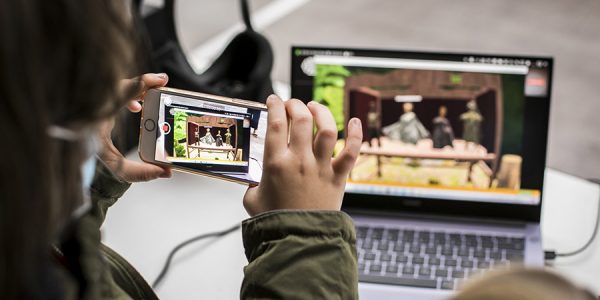 Eine Person filmt mit einem Handy einen Laptopbildschirm ab, auf dem ein Puppenspiel gezeigt wird.