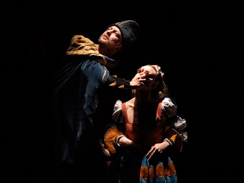 Ein Mann und eine Frau in historischen Gewändern, beide in dramatischer Pose vor schwarzem Hintergrund.