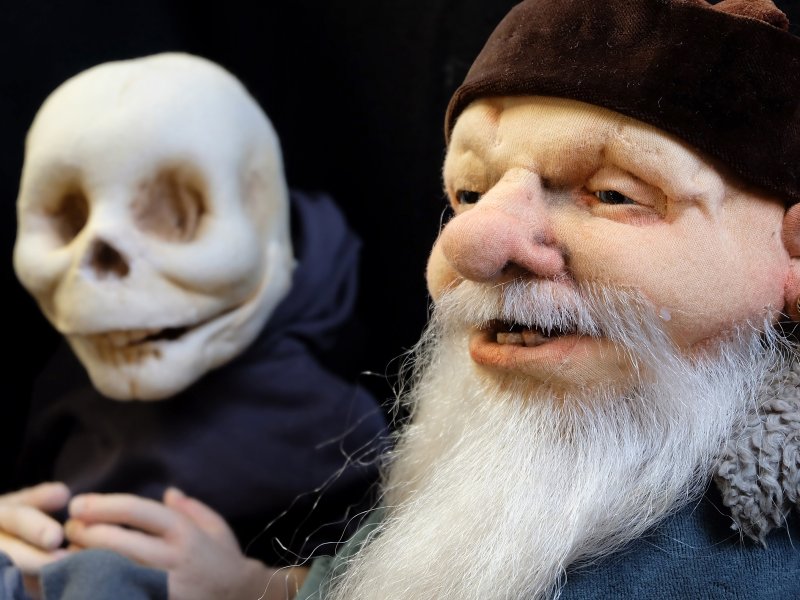 Detailreiche Puppen: Eine alte, bärtige Figur mit einer Mütze neben einer schädelähnlichen Puppe mit dunklem Umhang.