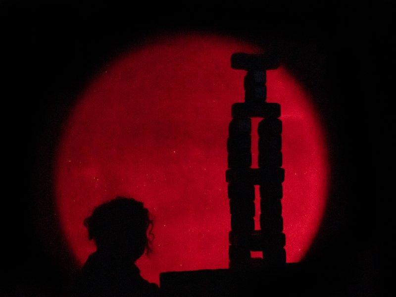 Silhouette einer Person vor einem großen roten Mond, während sie einen Turm aus Kohle aufbaut.